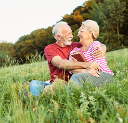 woman man outdoor senior couple happy lifestyle retirement together smiling love reading nature book sitting grass