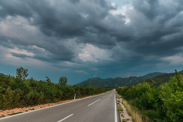 Asphalt road panorama in countryside on cloudy day. Road in forest under dramatic cloudy sky. Image of wide open prairie with a paved highway stretching out as far as the eye can see. - 671265223