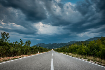 Asphalt road panorama in countryside on cloudy day. Road in forest under dramatic cloudy sky. Image of wide open prairie with a paved highway stretching out as far as the eye can see. - 671265231