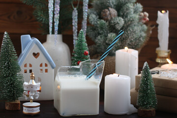 A New Year's house with a burning candle inside. Christmas decorations on a wooden tray with burning candles and a glass of milk