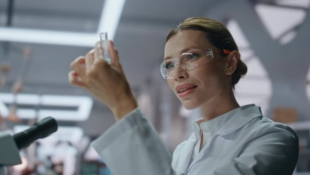 Smiling microbiologist examining test tube with medicines in laboratory closeup.
