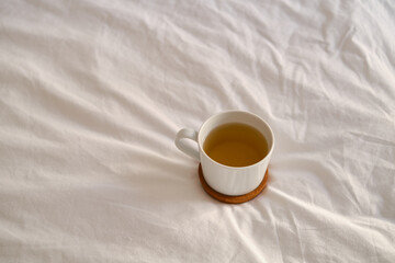 White cup with coffee or tea on the bed. Cozy morning photo. The concept is cozy and warm. Place for text
