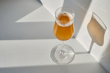 A glass of white wine, a cocktail in the rays of the sun on a light background. Celebrate and enjoy the moment. Tasting of alcoholic drinks. Glass of wine close up
