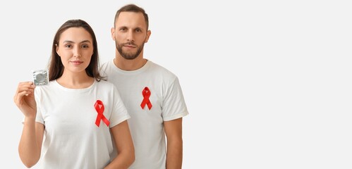 Young couple with red awareness ribbons and condom on light background with space for text. Banner for World AIDS Day - obrazy, fototapety, plakaty