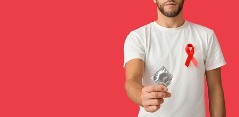 Young man with awareness ribbon and condom on red background with space for text. Banner for World AIDS Day