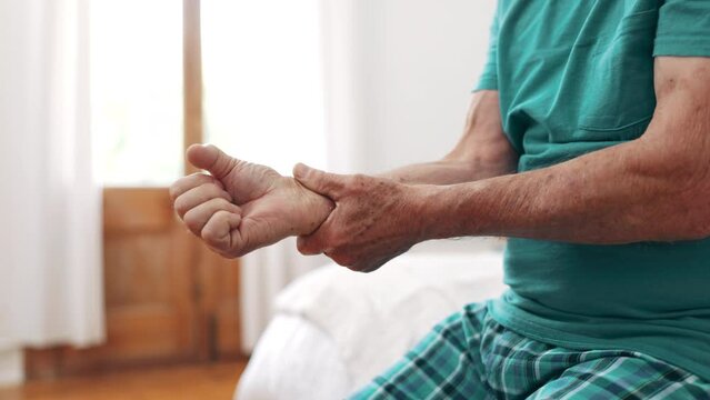 Arthritis, hands and elderly man with wrist pain, injury and inflammation with bruise, home and broken. Zoom, pensioner and senior guy on a bed, fingers with ache and closeup with sprain and strain