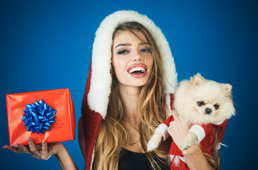 Christmas woman with little dog and gift box. Smiling girl in fur hat with Pomeranian Spitz in Santa Claus costume and Christmas present. Christmas and New year celebration. Pet and winter holidays.