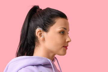 Young woman with hearing aid on pink background, closeup