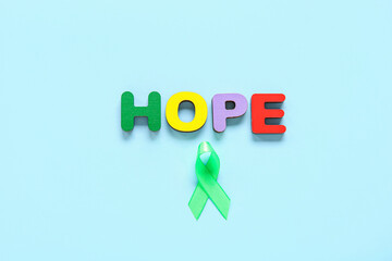 Green awareness ribbon and word HOPE made of wooden letters on blue background. Mental Health Day