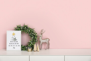 Christmas calendar with wreath and decor on drawers near pink wall - obrazy, fototapety, plakaty