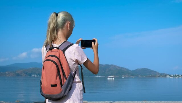 A tourist takes pictures on a smartphone. The girl photographs the sea landscape with a smartphone.