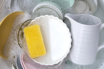 Dishes and bowls in water and bubbles of dishwashing liquid. Kitchen work