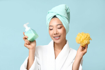 Young Asian woman with shower gel and loofah on blue background