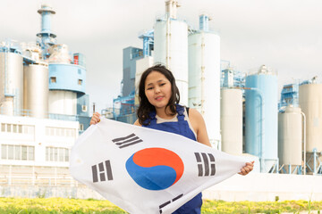 Positive young woman posing with South Korea flag in hands against background of factory