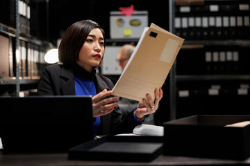 Asian private detective in agency file cabinet room reading criminal case file details....