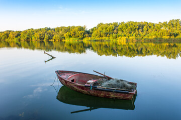 Obraz premium Wooden fishing boat in calm river water, Old traditional wooden boats, boat and paddle in still lake water, boat Moored Pier side River, Reflection of boat and sky sunset in Jijel a Algeria Africa.