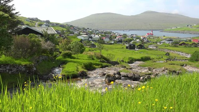 FAROE ISLANDS - JULY.16.2023 - Excellent aerial footage circling a coastal village on a green field in Sandavagur of the Faroe Islands.