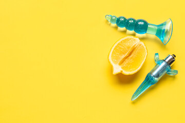 Different anal plugs from sex shop and half of tasty lemon on yellow background