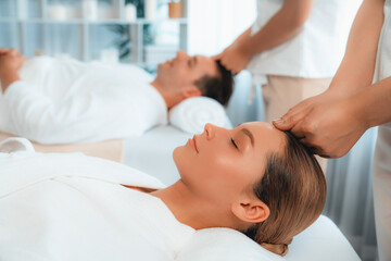 Fototapeta na wymiar Caucasian couple enjoying relaxing anti-stress head massage and pampering facial beauty skin recreation leisure in dayspa modern light ambient at luxury resort or hotel spa salon. Quiescent