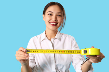 Female Asian decorator with tape measure on blue background
