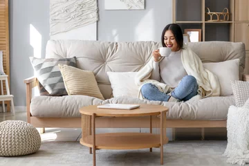 Foto op Canvas Young Asian woman with warm plaid drinking tea at home © Pixel-Shot