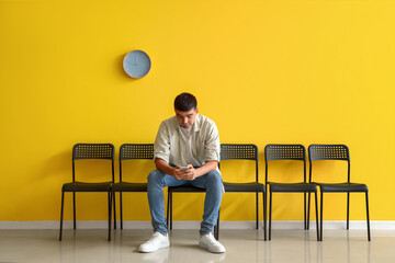 Young man with mobile phone waiting for his turn in room - obrazy, fototapety, plakaty