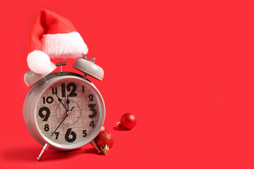 Alarm clock with Santa hat and Christmas balls on red background