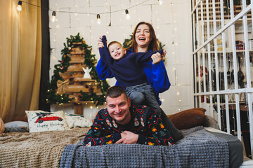 A happy family couple with a child in New Year locations. New Year's festive mood in the family circle. Christmas decorations in the bedroom. New Year. Christmas decorations at home