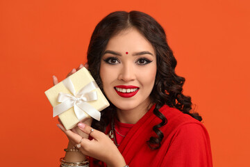 Beautiful Indian woman in sari with gift box on orange background