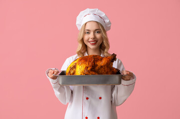 Young female chef with tasty baked turkey on pink background. Thanksgiving Day celebration