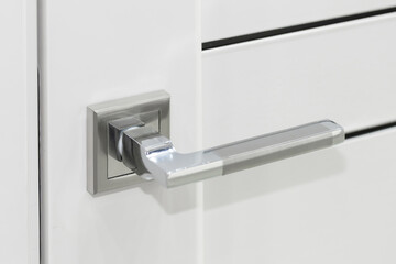 Chrome door handle on a closed white interior door, close-up. Modern door fittings. Minimalism in design. Interior accessories for apartments or offices. Modern door handle
