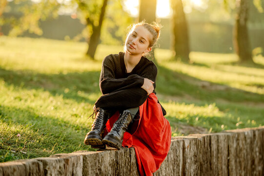Beautiful teenager girl in red skirt sitting in park outdoors at nature. Pretty teen model in trendy clothes at street