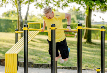 Man doing push ups with horizontal bar outdoors in park for healthy wellbeing. Sportsman guy making strong workout for muscle