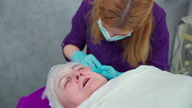 Beautician performs subcutaneous injections on elderly woman's face