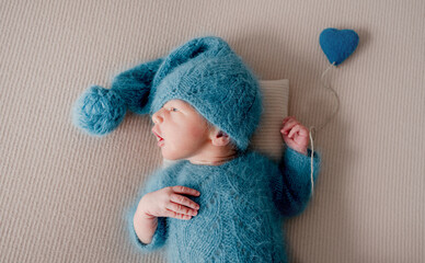 Adorable newborn baby boy in knitted hat and clothes holding heart toy and looking back. Cute...