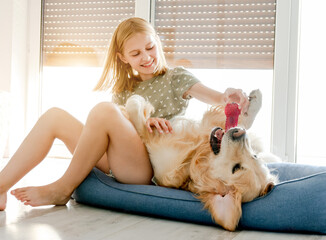 Cute preteen child girl with golden retriever dog playing at pillow at floor together. Pretty...