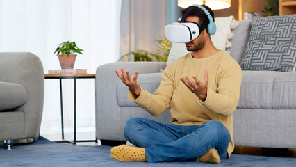 Lounge, virtual reality glasses and man with connection, gaming and headphones with stress relief. Person, home or player with esports, online gaming or VR eyewear with metaverse, futuristic or relax © Lumeez Ismail/peopleimages.com