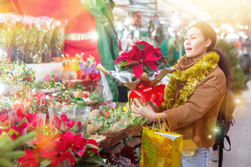 Asian woman choosing poinsettia while standing at christmas gift shop.