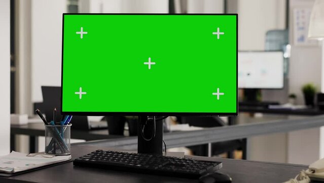 Greenscreen on office workstation placed in creative agency space, empty desk with pc running isolated mockup template. Computer desktop showing blank chromakey monitor display.