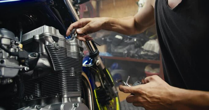 Close-up shot of a man using his strong, sinewy hands to tighten a nut and repair a motorcycle using a hex tool in his garage workshop