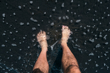 Close-up of Male Legs on Sandy Beach with Seawater Washing Over His Feet