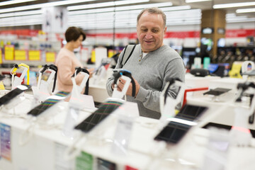 Fototapeta na wymiar Attentive European man chooses a mobile phone in an electronics store to buy it