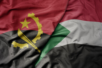 big waving national colorful flag of angola and national flag of sudan .