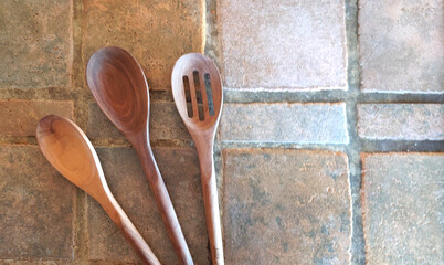 Three walnut wood food prep kitchen spoons on a rustic porcelain tiled countertop
