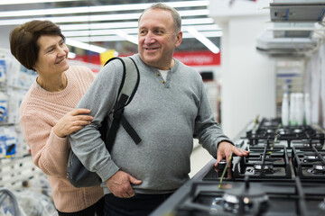 Happy spouses of mature age, who came to the electronics and home appliances store, choose a gas stove to buy it