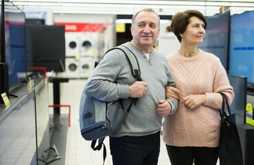 Fototapeta na wymiar Happy spouses of mature age are walking through the departments of an electronics and household appliances store
