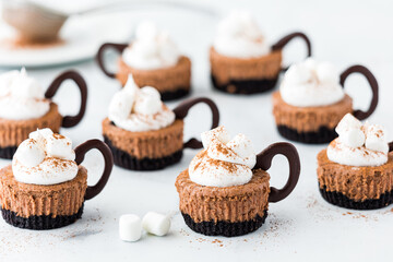 Hot cocoa mini cheesecakes topped with whip cream and marshmallows. - obrazy, fototapety, plakaty