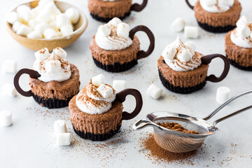 mini cheesecakes in the shape of cups of hot cocoa with cream and marshmallows.