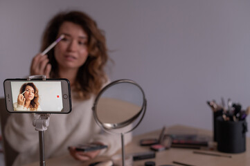 Caucasian woman leads an online make-up lesson for herself on her mobile phone