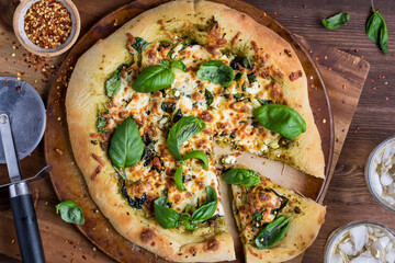 Above view of a homemade gourmet pesto and spinach pizza with chili peppers.